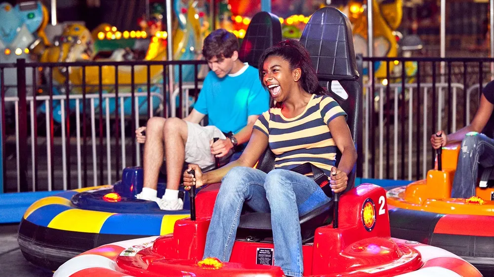 A guest smiling while riding a red-and-white Spin Zone bumper car at an indoor family entertainment center